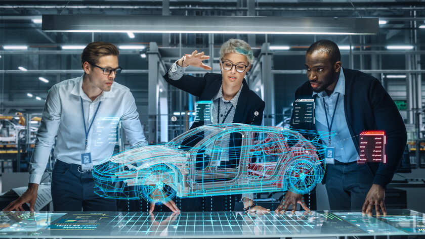 Diverses Team aus Industriedesignern diskutiert technologische Autoentwicklung mithilfe Augmented Reality Hologramm in Fabrik.