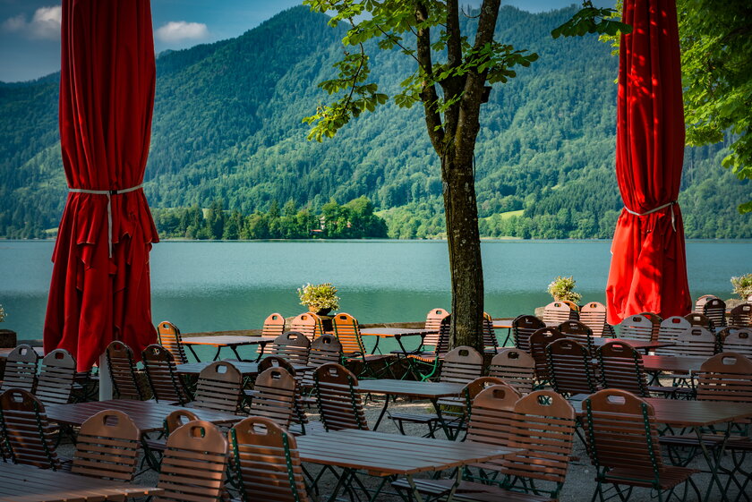 Biergarten Freisitz an einem bayrischen See vor bewaldeter Bergkulisse.