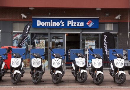 Blick auf Domino's Pizza Store mit mehreren Domino's Pizza Motorrollern