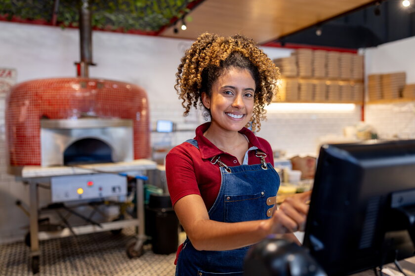 Bild Pizza Franchise Franchisenehmerin mit wilden Locken steht gluecklich in ihrer Pizzeria.