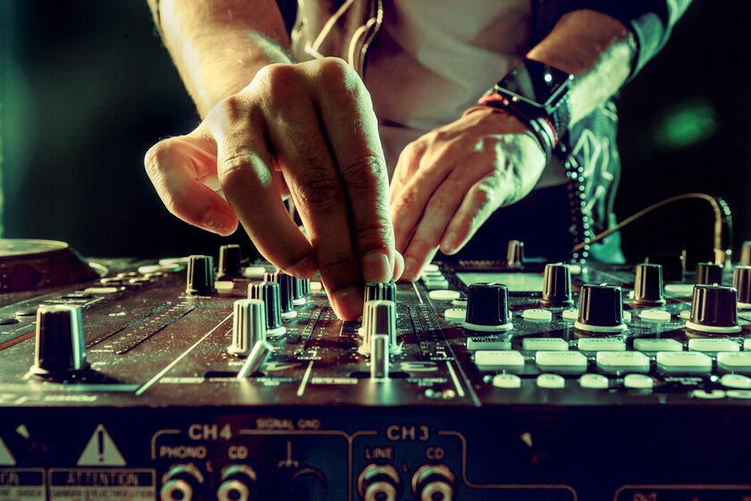 Nahaufnahme eines Mischpults, an dessen Regler zwei DJ-Hände nach dem perfekten Sound suchen.