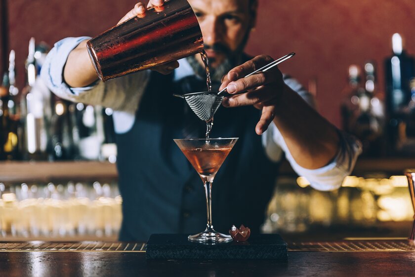 Barkeeper in Uniform bei der Zubereitung eines Cocktails hinter dem Tresen einer Bar.