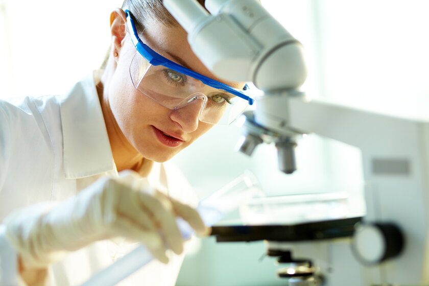 Biochemikerin im Labor experimentiert mit Substanzen unter dem Mikroskop.