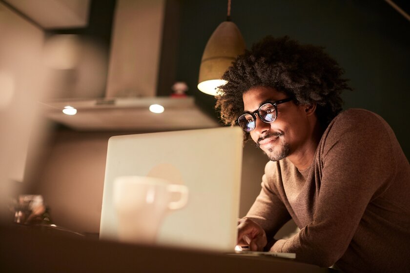 Bild Onlinerecherche Afroamerikaner arbeitet nachts in seiner Wohnung am Laptop.