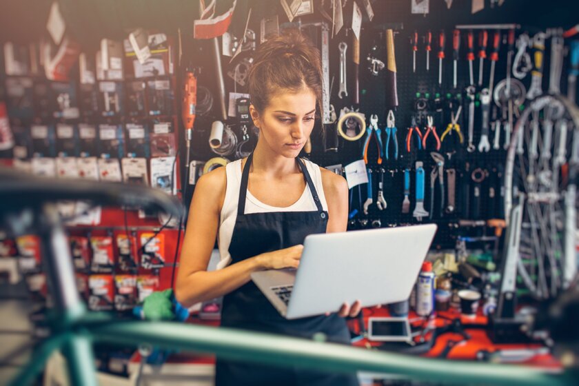 Bild Fahrradwerkstatt Junge Frau in Fahrradwerkstatt bei Onlinesuche am Rechner.