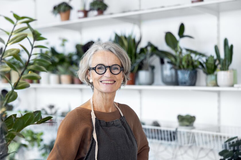 Lächelnde Unternehmerin steht inmitten von Pflanzen in ihrem Blumengeschäft.