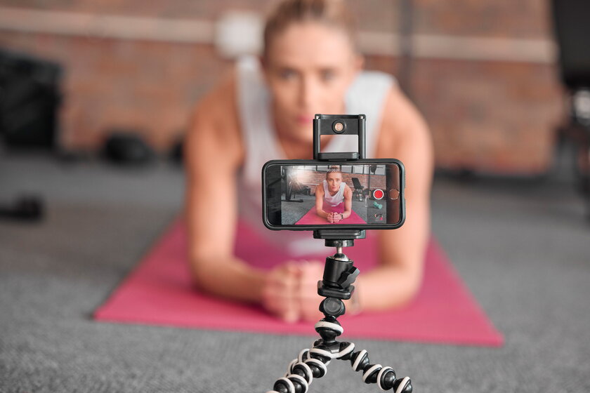 Fitness Influencerin im Liegestuetz auf Bodenmatte dreht ein Video.