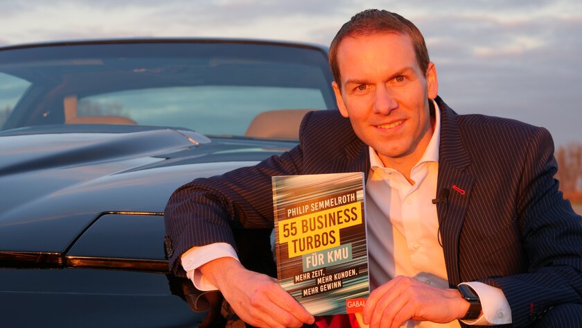 Philip Semmelroth präsentiert sein Buch „55 Business Turbos für KMU“ augenzwinkernd neben einem Sportwagen.