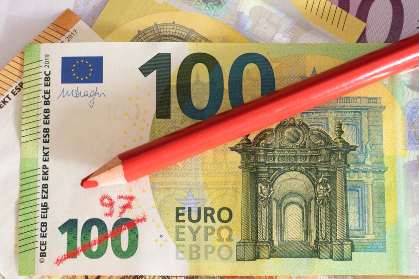 Rotstift der Inflation auf einem Hundert-Euro-Schein, hat den Wertbetrag durchgestrichen und durch reduzierten Betrag korrigiert.
