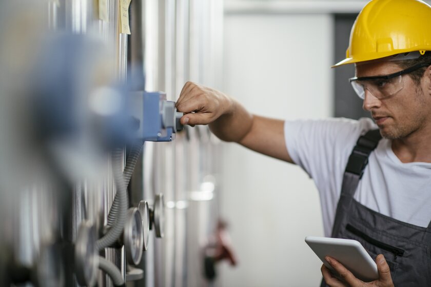 Mann mit Tablet befindet sich in einer Erdgasverarbeitungsanlage und kontrolliert Systemanlagen.