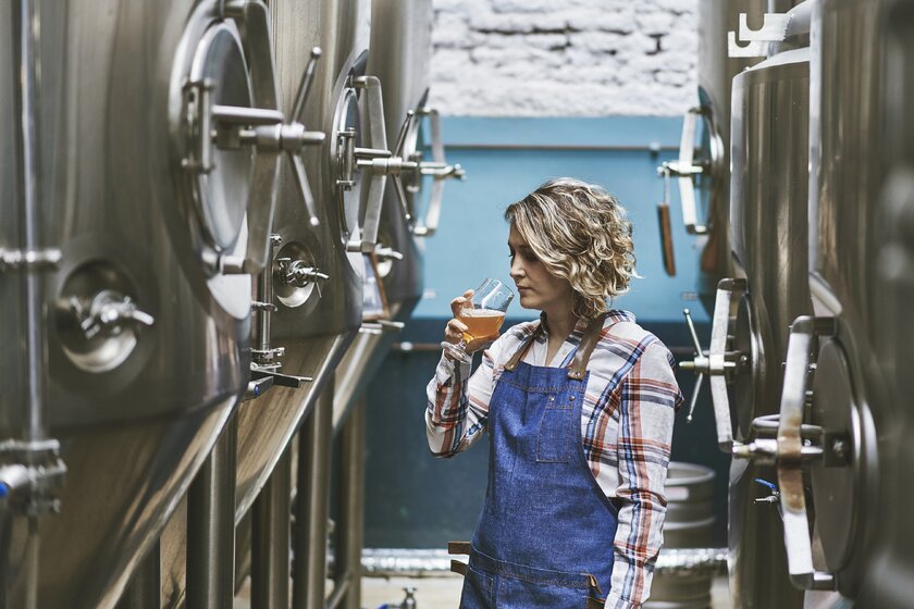 Jungunternehmerin steht in Brauereianlage und verkostet Bier. Jungunternehmerin steht in Brauereianlage und verkostet Bier.