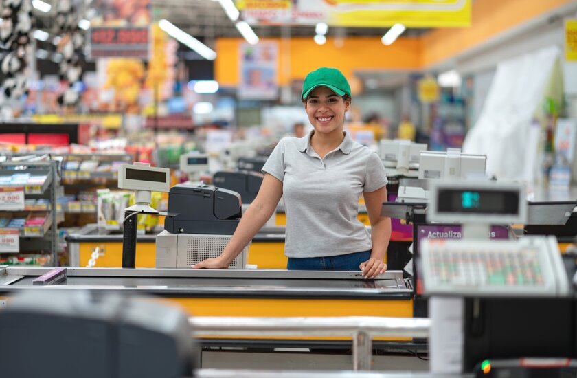 Freundlich lächelnde Kassiererin mit Migrationshintergrund in einem Baumarkt steht an ihrer Kasse.