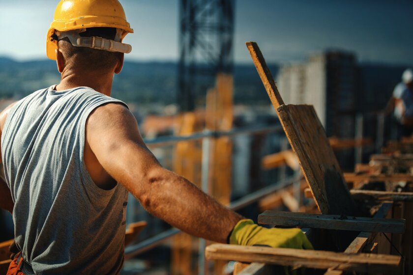 Bauarbeiter auf einem hohen Gebäude blickt über Kräne und Dächer.