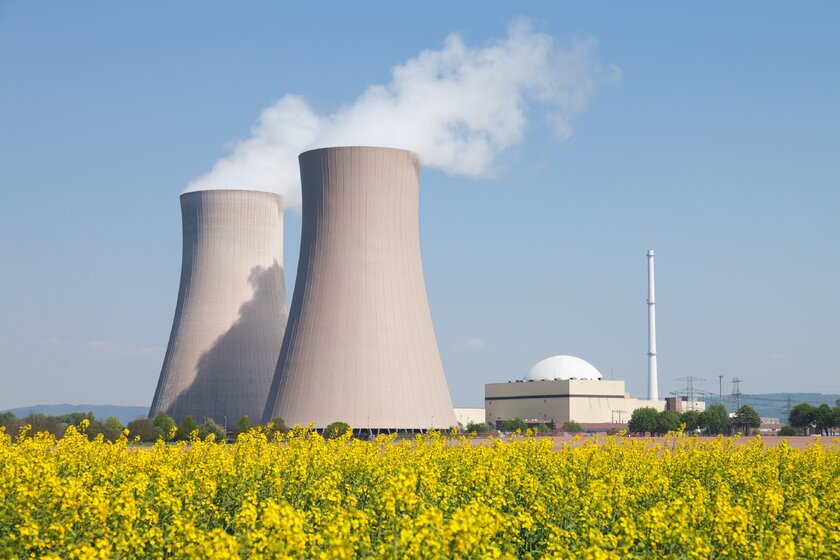 Atomkraftwerk mit dampfenden Kühltürmen, im Vordergrund ein Rapsfeld.