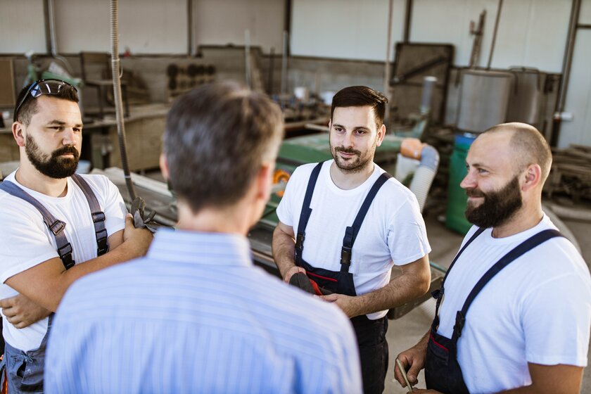 Teambesprechung zwischen Chef und Mitarbeitenden in einem kleinen Handwerksbetrieb.