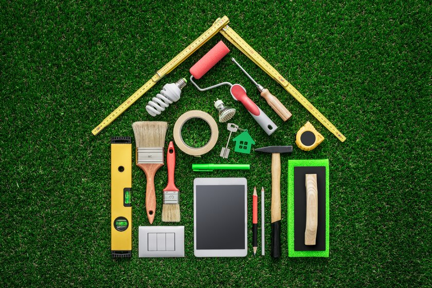Verschiedene Werkzeuge angeordnet auf einem Rasen bilden ein Haus.