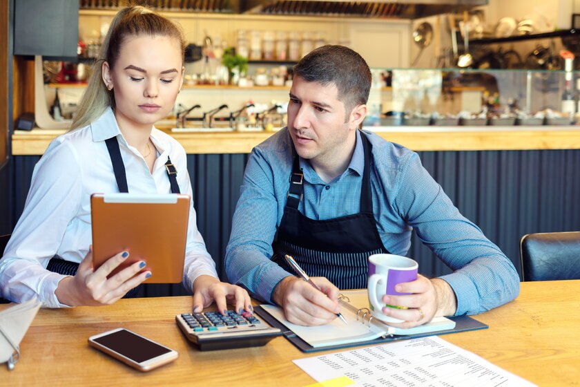 Junge Familienrestaurantbesitzer diskutieren Finanzierung bei Berechnung von Einnahmen und Ausgaben.