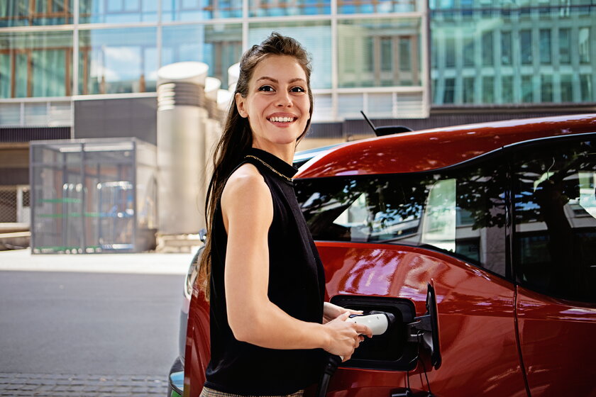 Portrait einer Frau mit ihrem Elektrofahrzeug an der Ladestation.