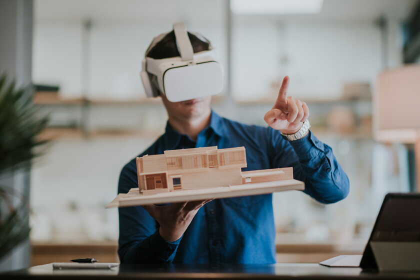 Architekt mit VR-Brille und Baumodell in der Hand nutzt neue Technologien und erkundet virtuell sein Projekt.