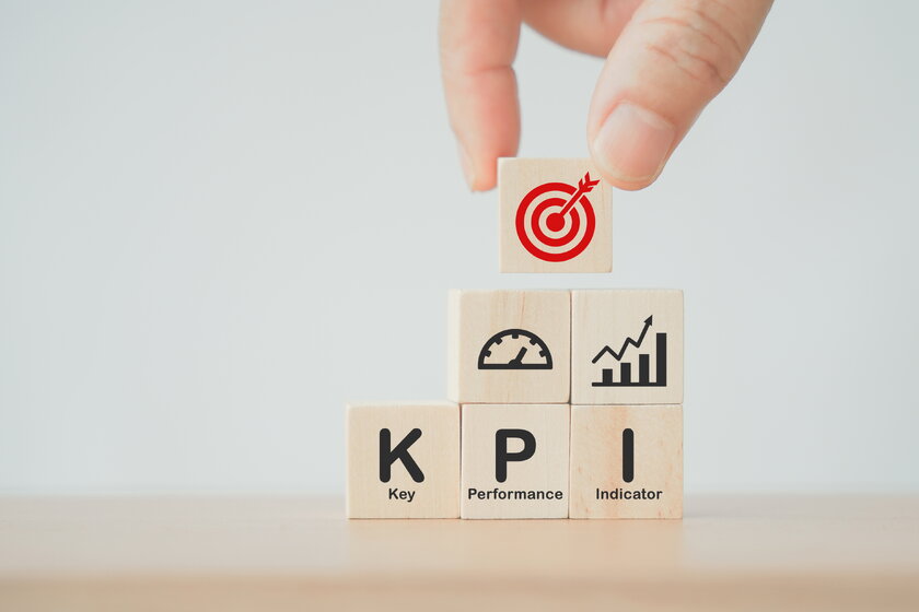 Bild KPI Spielsteine Hand greift nach einem Spielstein mit aufgemalter Zielscheibe, darunter befinden sich noch mehr Spielsteine mit Aufschrift KPI.