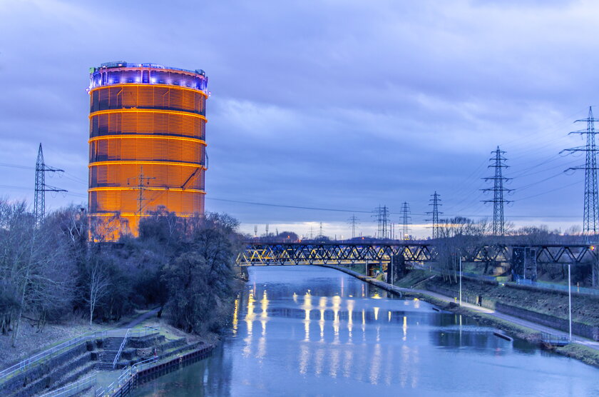 Blick auf den Gasometer in Oberhausen am Kanalufer bei Nacht.