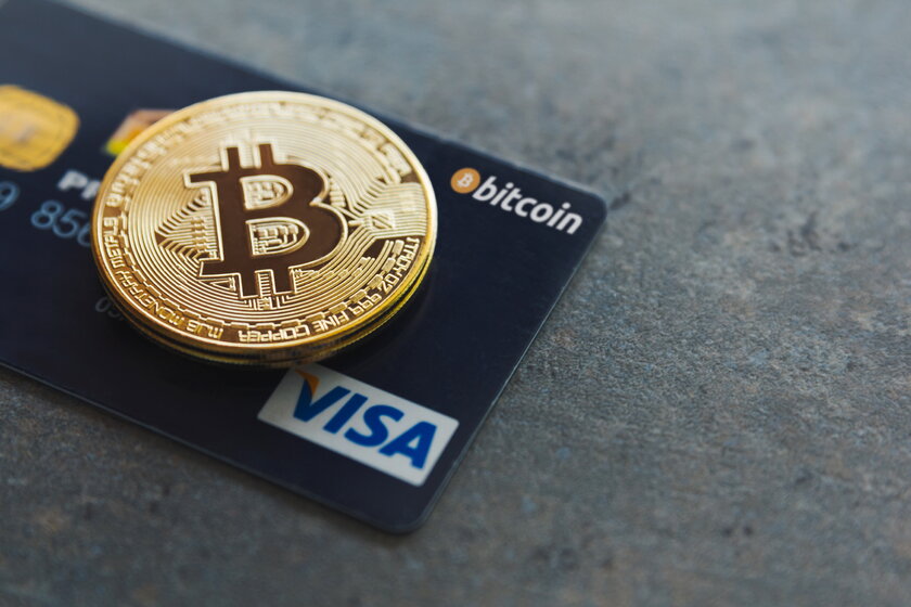 Ein Bitcoin und eine Visa-Kreditkarte auf strukturiertem Hintergrund.