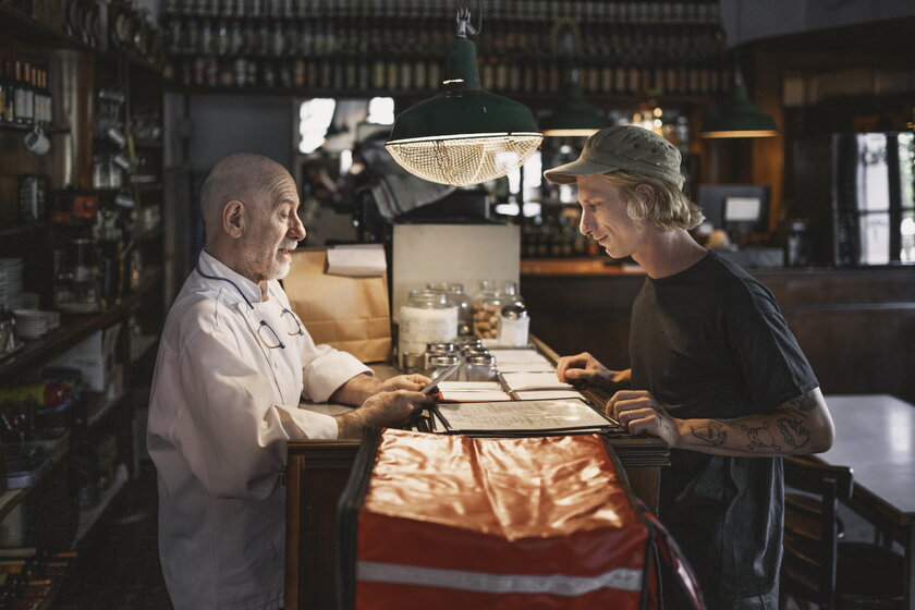 Restaurantbesitzer mit Lieferfahrer stehen am Tresen und gehen Bestellung durch.