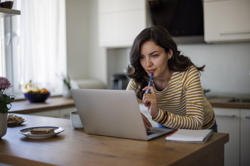 Junge Unternehmerin ist konzentriert im Homeoffice ueber Laptop gebeugt.