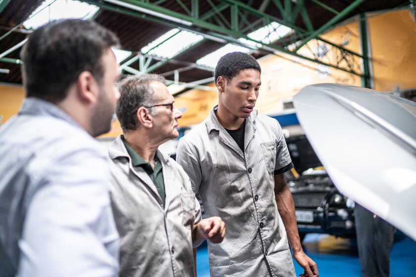 Bild Autowerkstatt Azubi und Lehrmeister begutachten Kundenauto in Werkstatt.