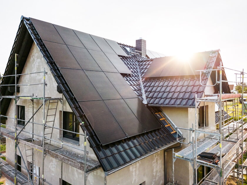 Baustelle eines Einfamilienhauses mit Sonnenkollektoren im Morgenlicht.