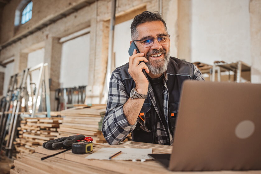 Tischlermeister am Telefon im Werkstattoffice arbeitet mit Laptop.