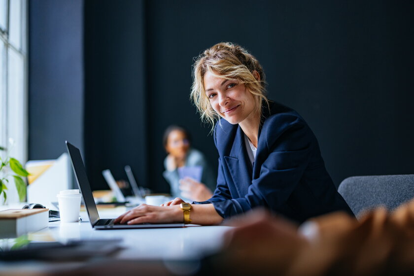 Laechelnde Freiberuflerin im Coworking Space arbeitet an ihrem Laptop.