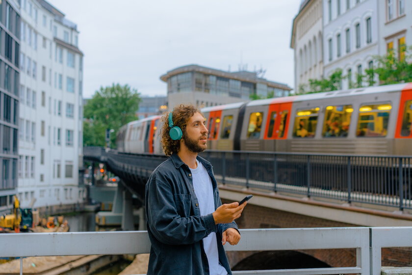 Mann mit Kopfhoerern vor vorbeifahrender Hamburger U-Bahn.