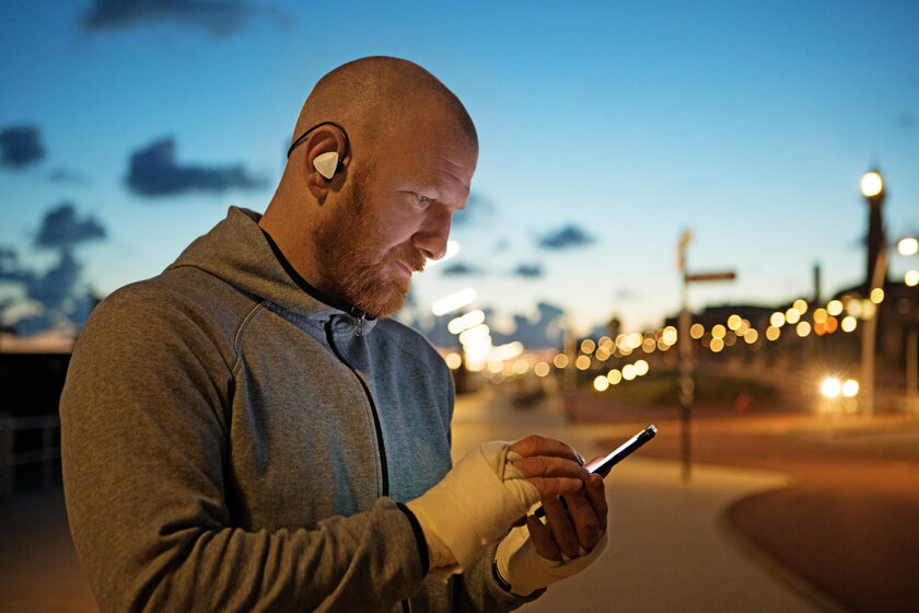 Sportlicher Mann mit Glatze und bandagierten Haenden am Smartphone