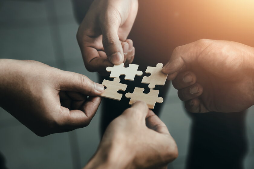 Bild Puzzleteile Vier Haende halten Puzzleteile und schliessen diese zu einem einzigen perfekten Team.
