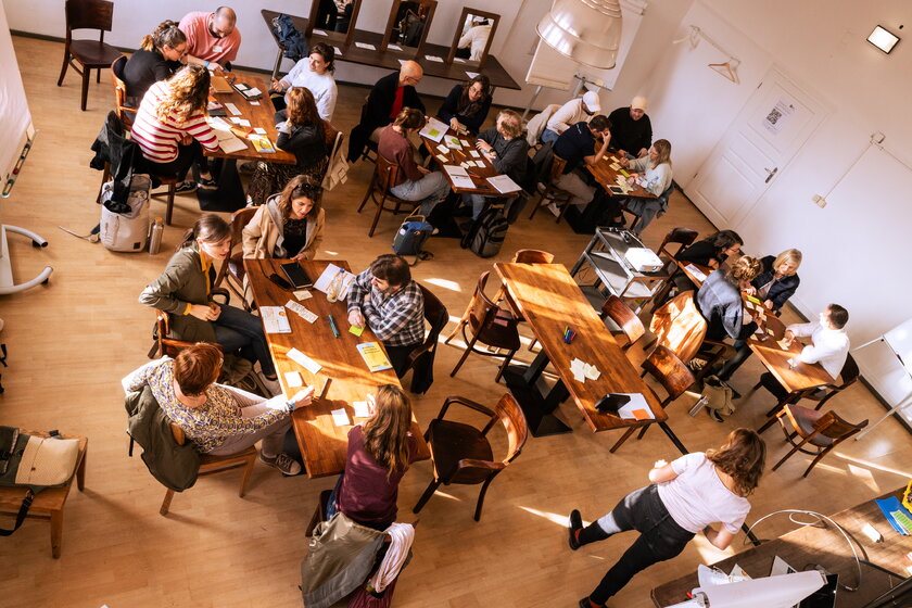 Bild Workshop Blick von oben auf zahlreiche Seminarteilnehmer an Tischen sitzend.