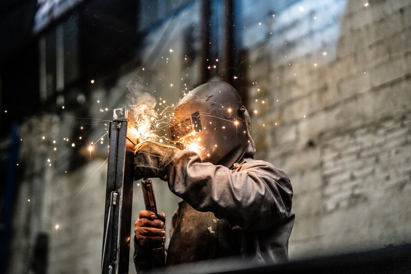 Bild Metallverarbeitung Ein Mann im Arbeitsanzug mit Schutzmaske beim Schweissen von Metall.