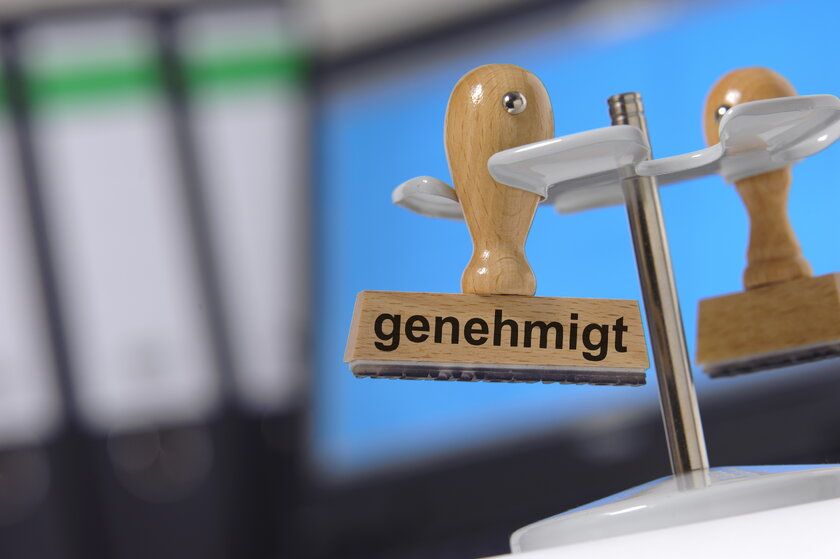 Nahaufnahme eines Holzstempels mit der Aufschrift Genehmigt vor Aktenhintergrund.