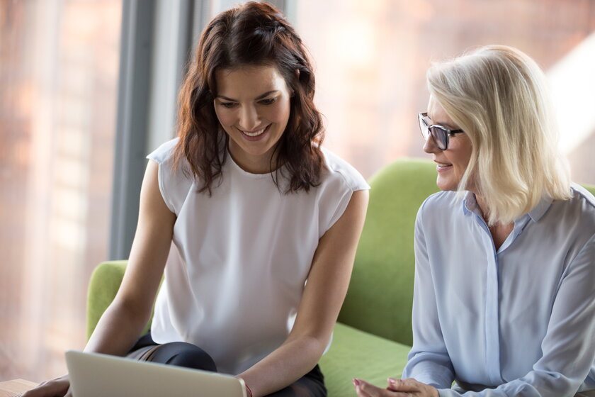 Junge Frau bespricht Businessplan am Laptop mit erfahrener Beraterin.