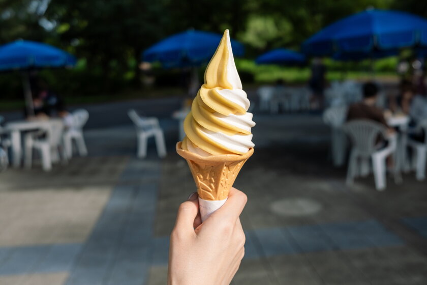 Hand mit Mango-Softeis vor Freisitzhintergrund.