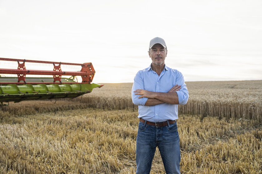 Landwirt, der am Ende eines langen Arbeitstages im Weizenfeld neben der Erntemaschine steht.