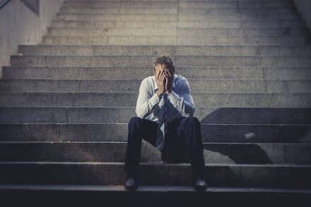 Mann sitzend auf Treppe, verdeckt verzweifelt Gesicht mit Händen