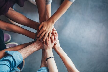unternehmensWert:Mensch wird verlängert Team von Mitarbeitern zeigt mit gemeinsamen Handabschlag Zusammenhalt im Team