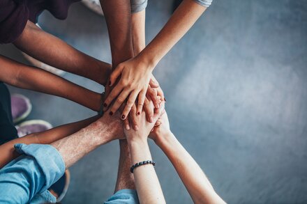 Team von Mitarbeitern zeigt mit gemeinsamen Handabschlag Zusammenhalt im Team