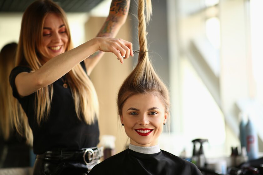 Bild Haare ab Friseur-Stylistin haelt langen Zopf ihrer Kundin nach oben und setzt die Schere an.