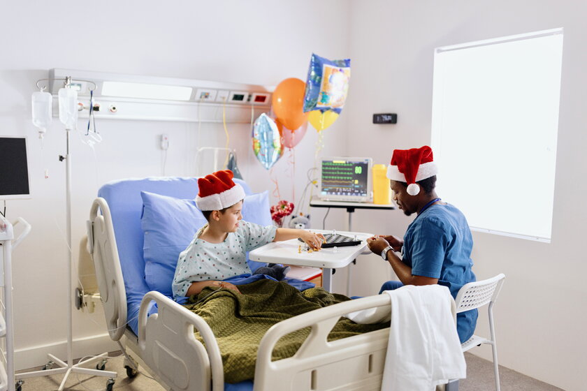 Krankenpfleger mit Nikolausmuetze spielt mit seinem Patienten im Krankenzimmer Schach.