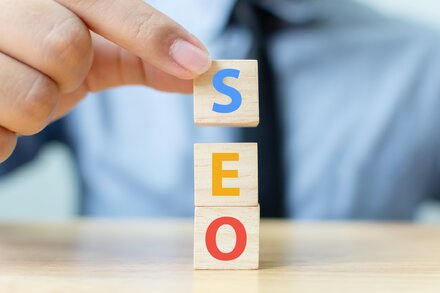 Nahaufnahme einer Hand eines Mannes, der mit Holzsteinen das Word SEO vertikal stapelt.