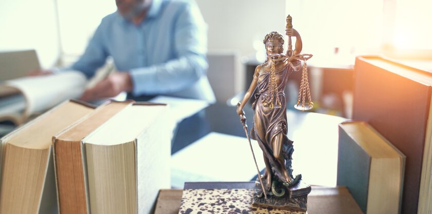 Anwalt am Schreibtisch, Justitia im Vordergrund.
