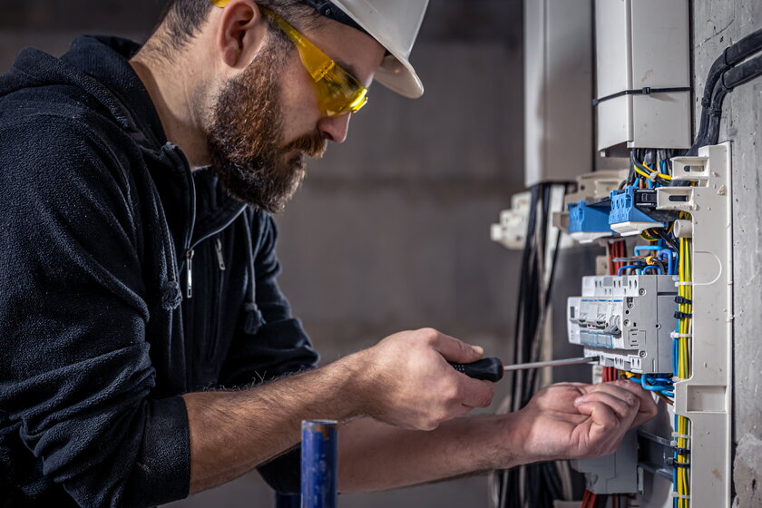 Elektrotechniker arbeitet in einer Schalttafel mit einem elektrischen Anschlusskabel.